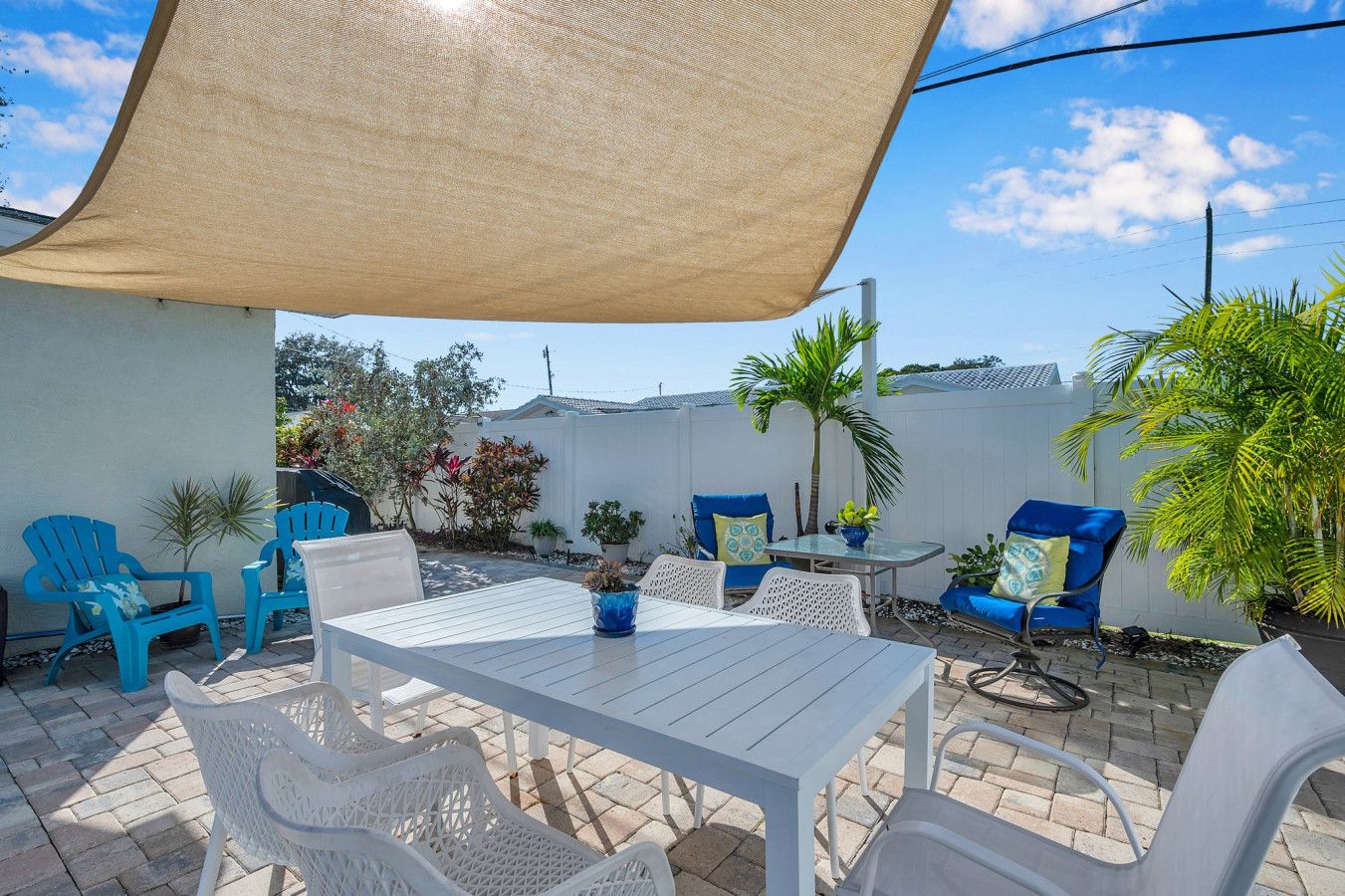 Un patio al aire libre con una mesa, sillas, zona sombreada y plantas en macetas.