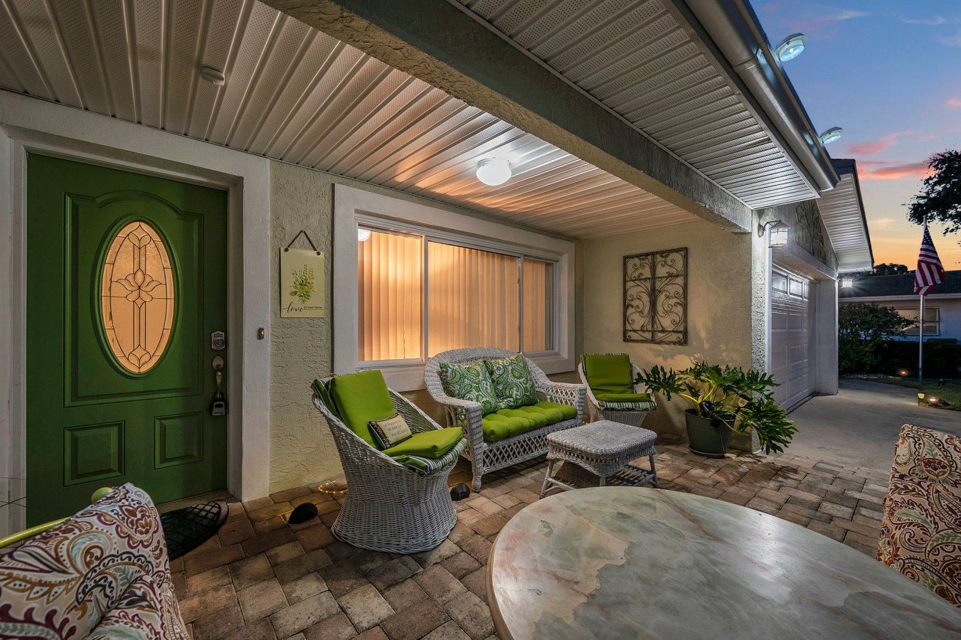 A covered patio with wicker furniture, a green door, and a view of the house in the background.