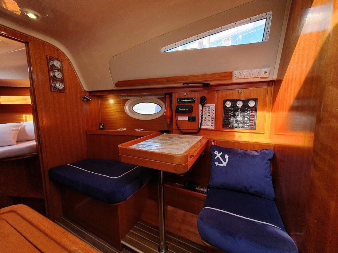 A compact cabin with a small table, two blue cushioned seats, a control panel, and a window.