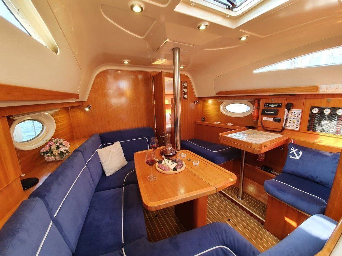 A boat interior with a dining area, blue upholstered seating, a table with a wine glass and plate, and a control panel.