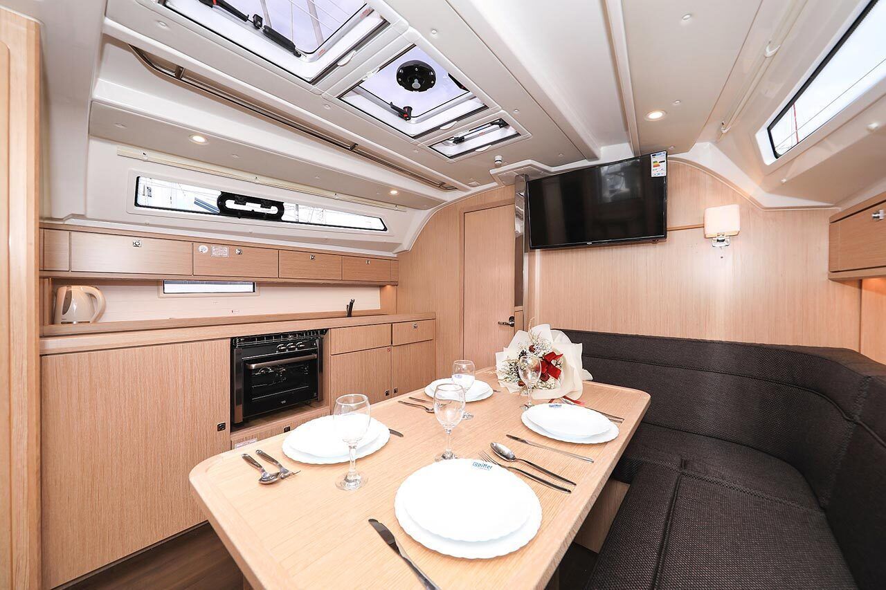 A compact kitchen with a built-in oven, a dining table set for four, and a flat-screen TV mounted on the wall.