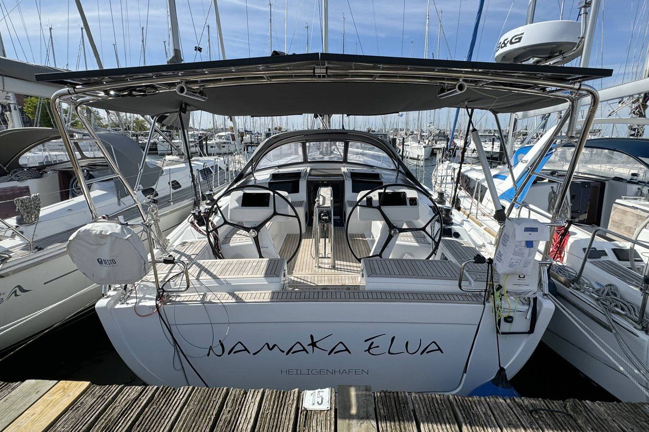 Eine Segelyacht namens 'NAMAKA ELUA' liegt in einer Marina mit weiteren Booten, einem Holzboden und wolkenlosem Himmel vor Anker.