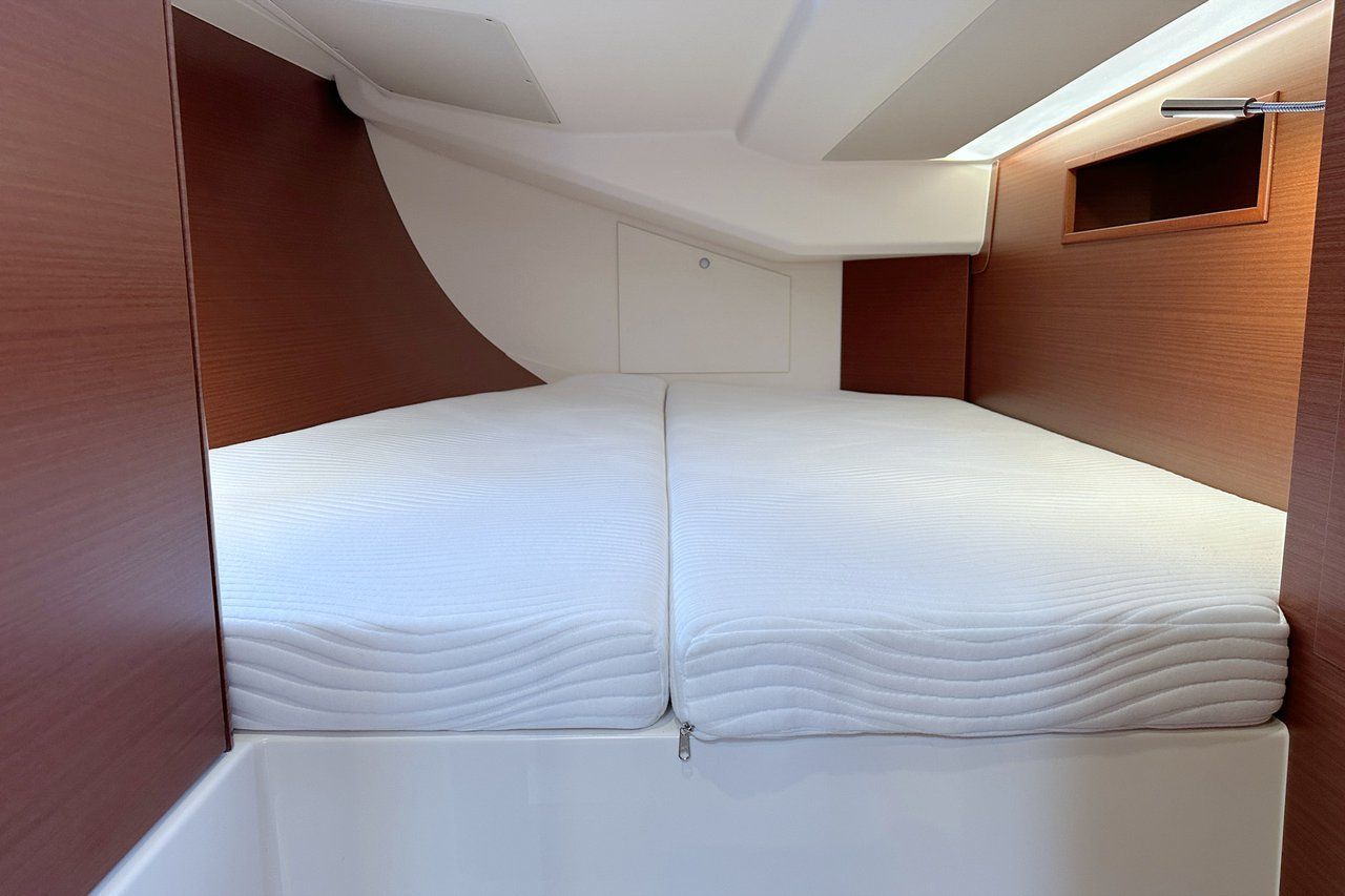 Ein kompakter, moderner Innenraum mit einem zentral platzierten Bett, einem kleinen Fenster und einer eingebauten Ablagefläche.
