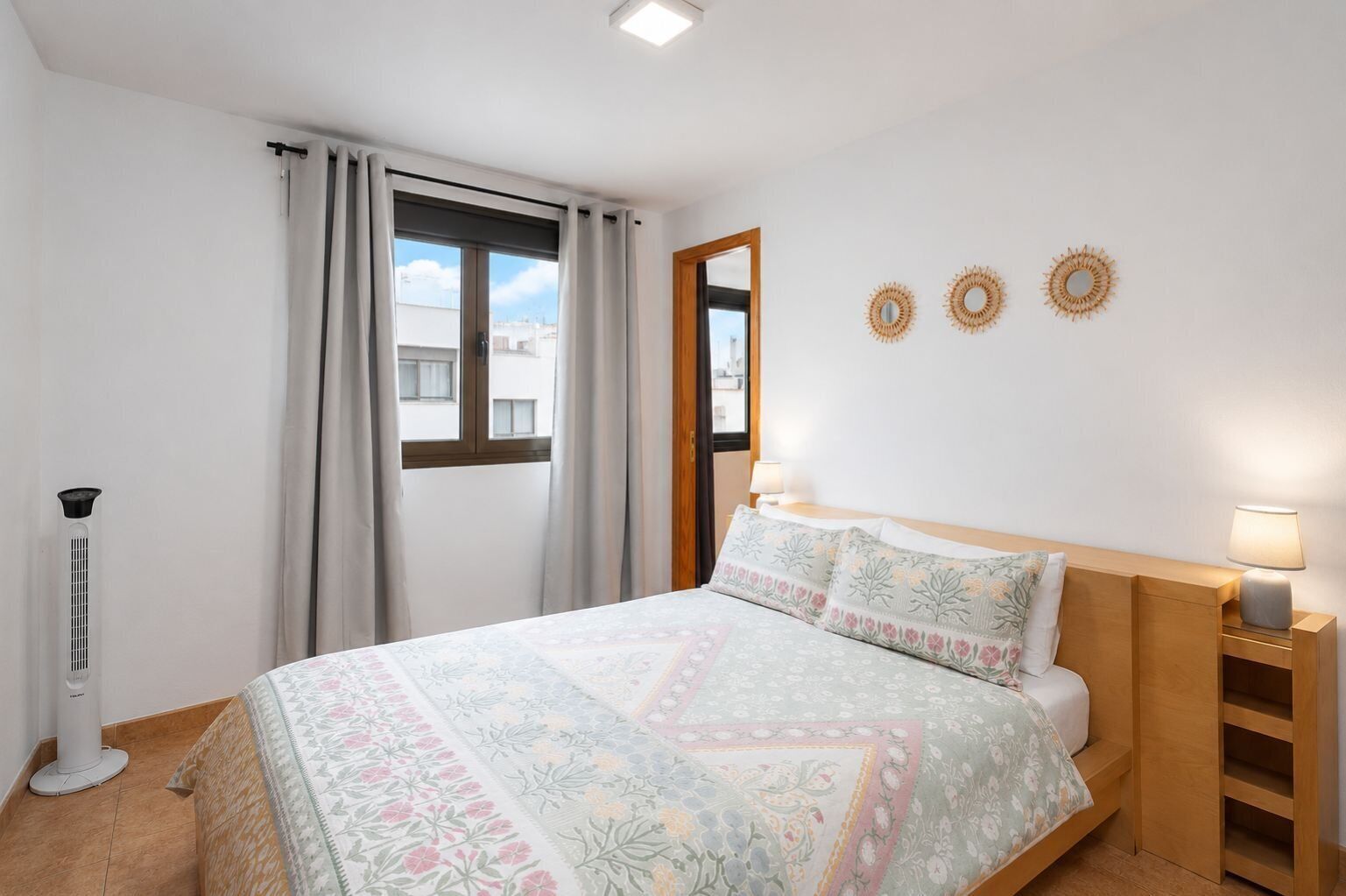 A bedroom with a bed, bedside lamps, a window with curtains, and wall decor.