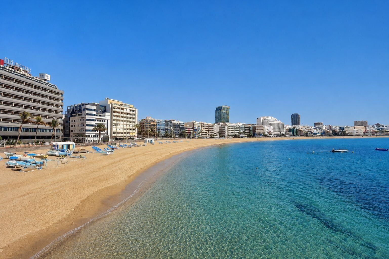 A beachfront hotel with multiple floors, a sandy beach, and clear blue water.