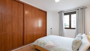A bedroom with a bed, a wardrobe, a window with curtains, and a radiator. - GuestReady - Las Canteras Shoreline (Las Palmas de Gran Canaria)