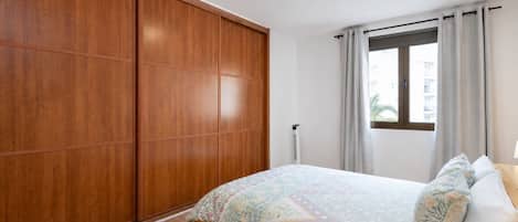 Un dormitorio con cama, armario, ventana con cortinas y radiador.