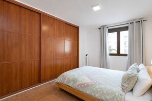A bedroom with a bed, a wardrobe, a window with curtains, and a radiator. - GuestReady - Las Canteras Shoreline (Las Palmas de Gran Canaria)