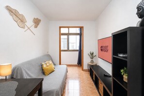 A modern living room with a grey sofa, a small table with a lamp, a TV on a black stand, and a window with a view. - GuestReady - Las Canteras Shoreline (Las Palmas de Gran Canaria)