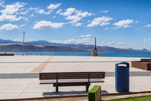 A bench and trash can in a public space with a view of a body of water and mountains. - GuestReady - Las Canteras Shoreline (Las Palmas de Gran Canaria)