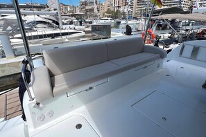 A boat's deck with a cushioned seating area, a control panel, and a lifebuoy. - Sun-Kissed Sailing Adventure in Islas Baleares, Mallorca (Palma)