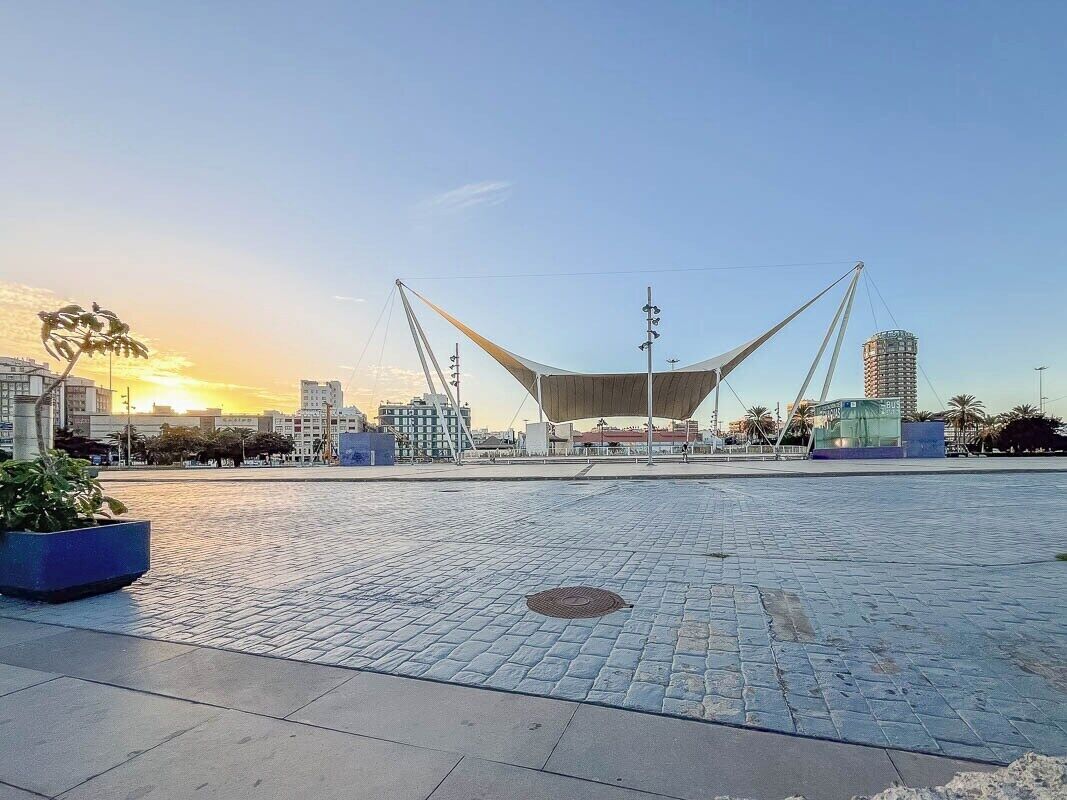 Una plaza abierta con una gran estructura moderna en forma de tienda, rodeada de edificios y un cielo despejado.