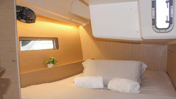 Una cabina compatta e ben illuminata con un letto singolo, una piccola finestra e un proiettore a parete.