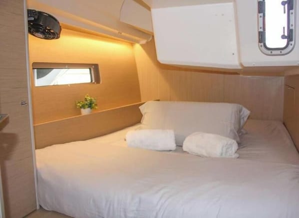 Een compacte, goed verlichte cabine met een enkel bed, een klein raam en een wandgemonteerde projector.