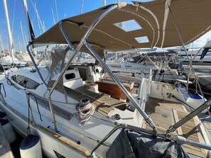 Een zeilboot afgemeerd in een jachthaven met een overdekt dek, meerdere masten en diverse apparatuur en opbergartikelen.