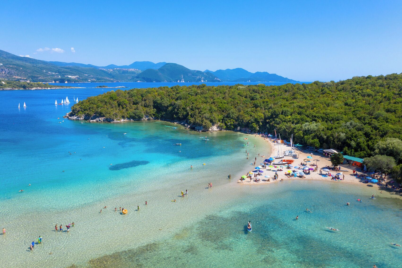 Una playa con aguas turquesas cristalinas, una orilla arenosa y una zona boscosa.