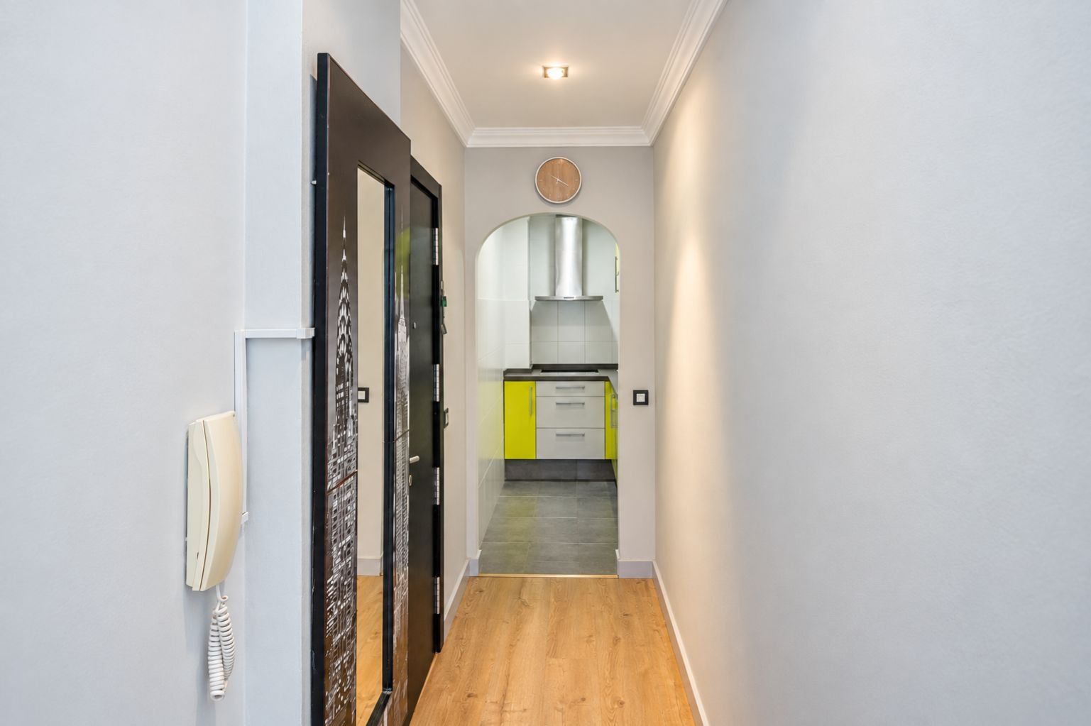 Um corredor com piso de madeira que leva a uma área de cozinha com armários amarelos e uma coifa de aço inoxidável.