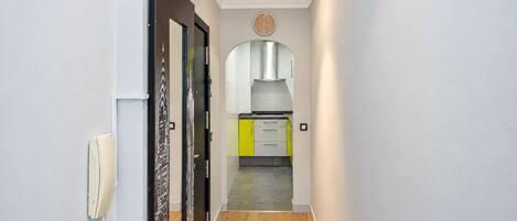 Un pasillo con piso de madera que conduce a una zona de cocina con armarios amarillos y un extractor de acero inoxidable.