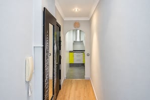 A hallway with a wooden floor leading to a kitchen area with yellow cabinets and a stainless steel range hood. - GuestReady - Orlando Panoramic Sea View (Las Palmas de Gran Canaria)