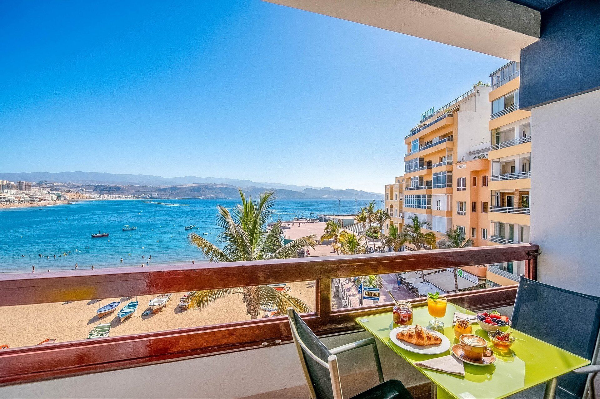 Un balcón con mesa listo para el desayuno con vista a la playa y al mar.