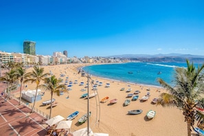 Ein Strand mit vielen Booten, blauem Meer und einer Stadtlandschaft im Hintergrund.