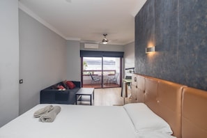 Ein Hotelzimmer mit Bett, Sofa, einem kleinen Tisch, einem Sessel, einem Balkon mit Aussicht und einem Deckenventilator.