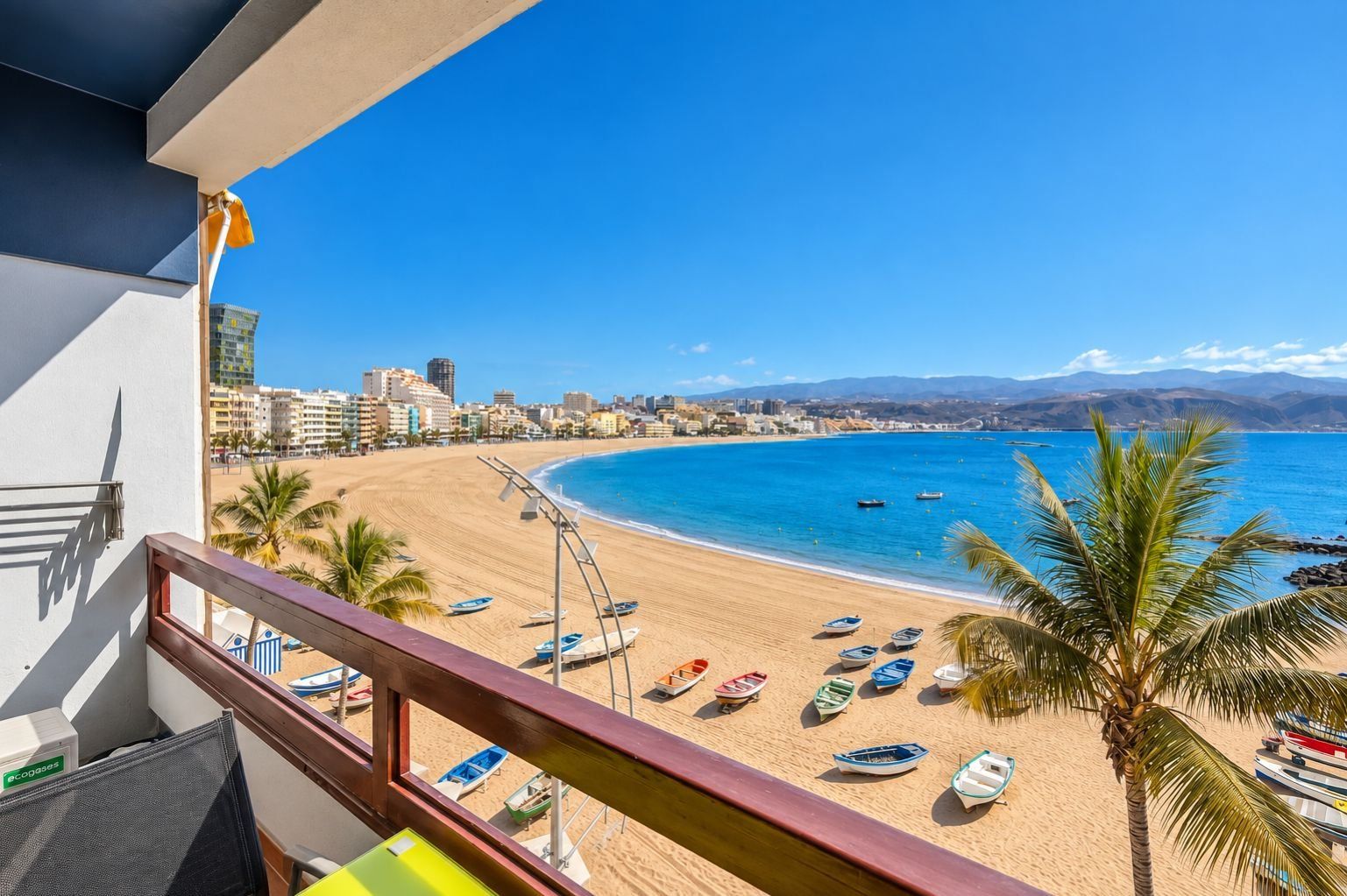 Un balcón con vista a una playa, barcos y un paisaje urbano.