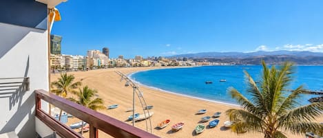 Un balcón con vista a una playa, barcos y un paisaje urbano.