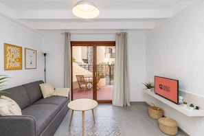 A modern living room with a grey sofa, a small round table, and a TV on a white shelf. - GuestReady - Duplex with Pool and Sunny Terrace (Parque Holandes)
