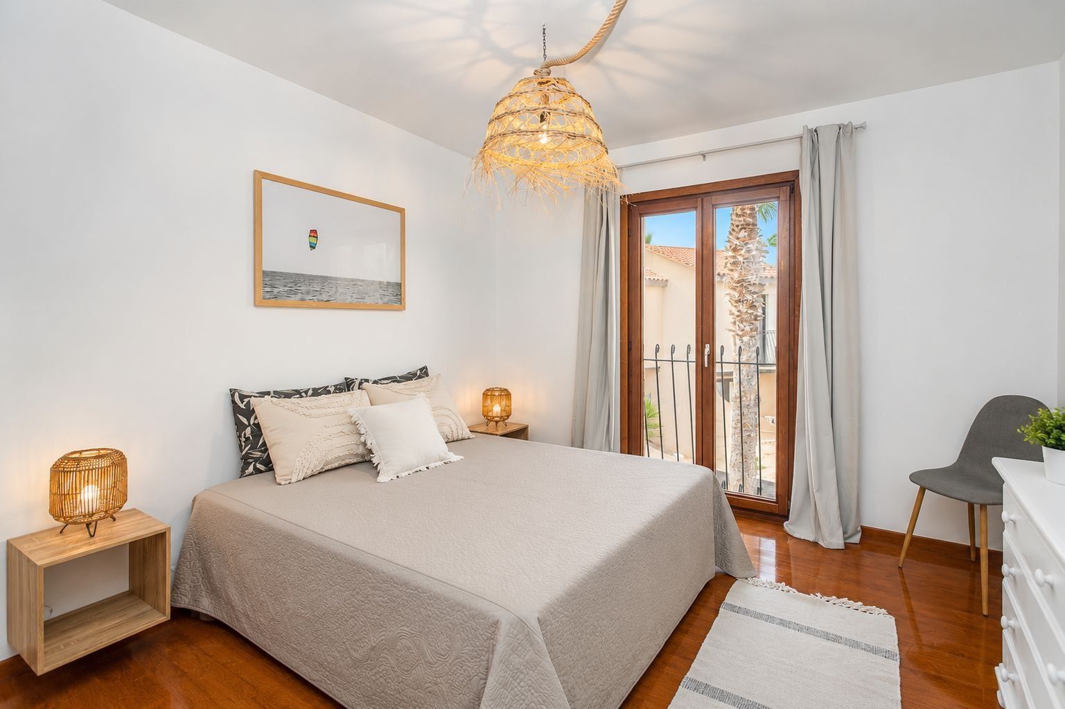 Une chambre à coucher avec un lit, des lampes de chevet, une fenêtre avec des rideaux, un balcon et une chaise.