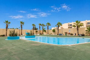 Ein Schwimmbecken mit Liegestühlen und Palmen, umgeben von einem Gebäude mit heller Fassade.