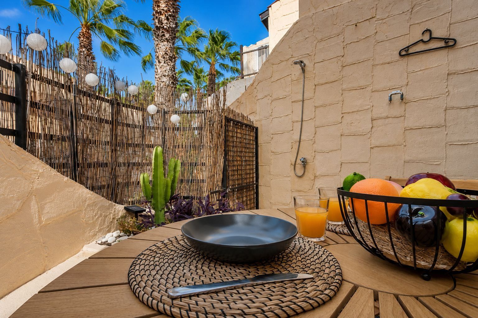 An outdoor dining area with a table set for two, a woven placemat, and a fruit basket.