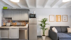 A modern kitchen with a built-in oven, a refrigerator, and a dishwasher. There is a gray sofa and a potted plant in the living area. - GuestReady - Duplex with Pool and Sunny Terrace (Parque Holandes)