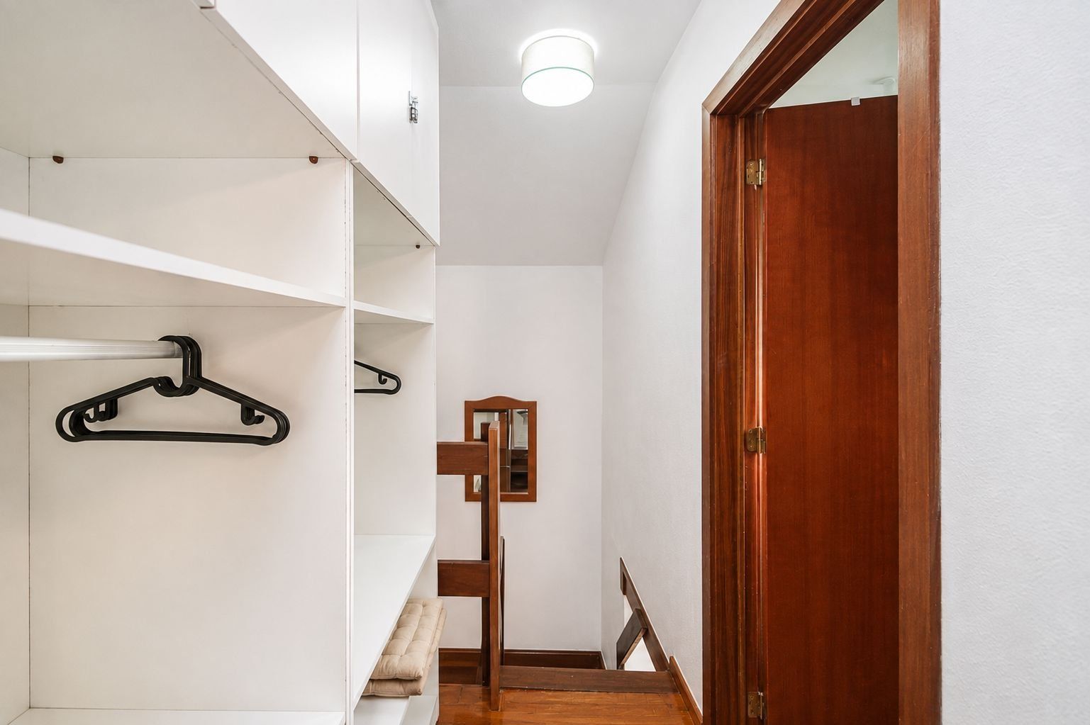 A hallway with a wooden door, white walls, and a hanging coat rack.