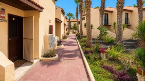 A corridor with palm trees and a red pathway leading to a building with a door marked 'CASAN'. - GuestReady - Duplex with Pool and Sunny Terrace (Parque Holandes)