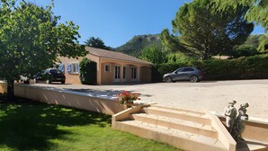 Un edificio con techo de tejas, una entrada por una calzada y un área verde con escalones que conducen a la entrada.