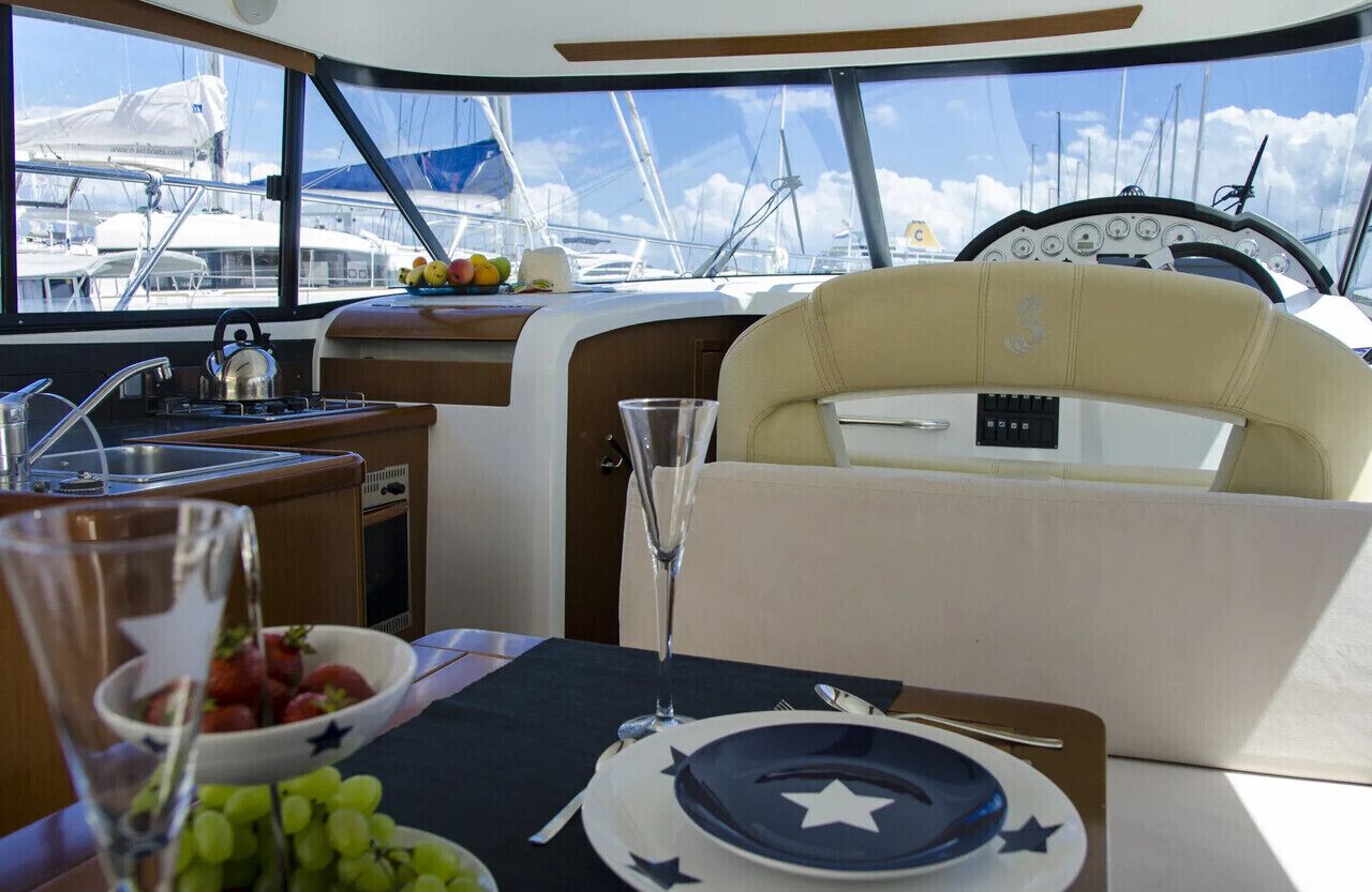 A yacht interior with a dining area, a kitchen, and a view of the marina.