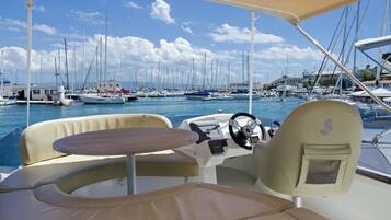 A boat's interior with a steering wheel, cushioned seating, and a table.