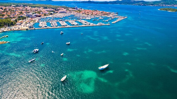 An aerial view of a coastal town with a marina, boats, and a clear blue sea. - Sun-Kissed Sailing Adventure in Zadar, Croatia (Biograd na moru)