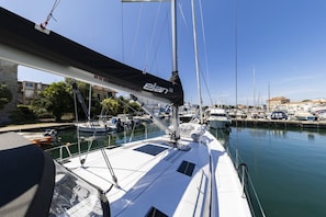 Een jachthaven met aangemeerde boten, een zeilboot met een zwart zeil, en een heldere lucht.