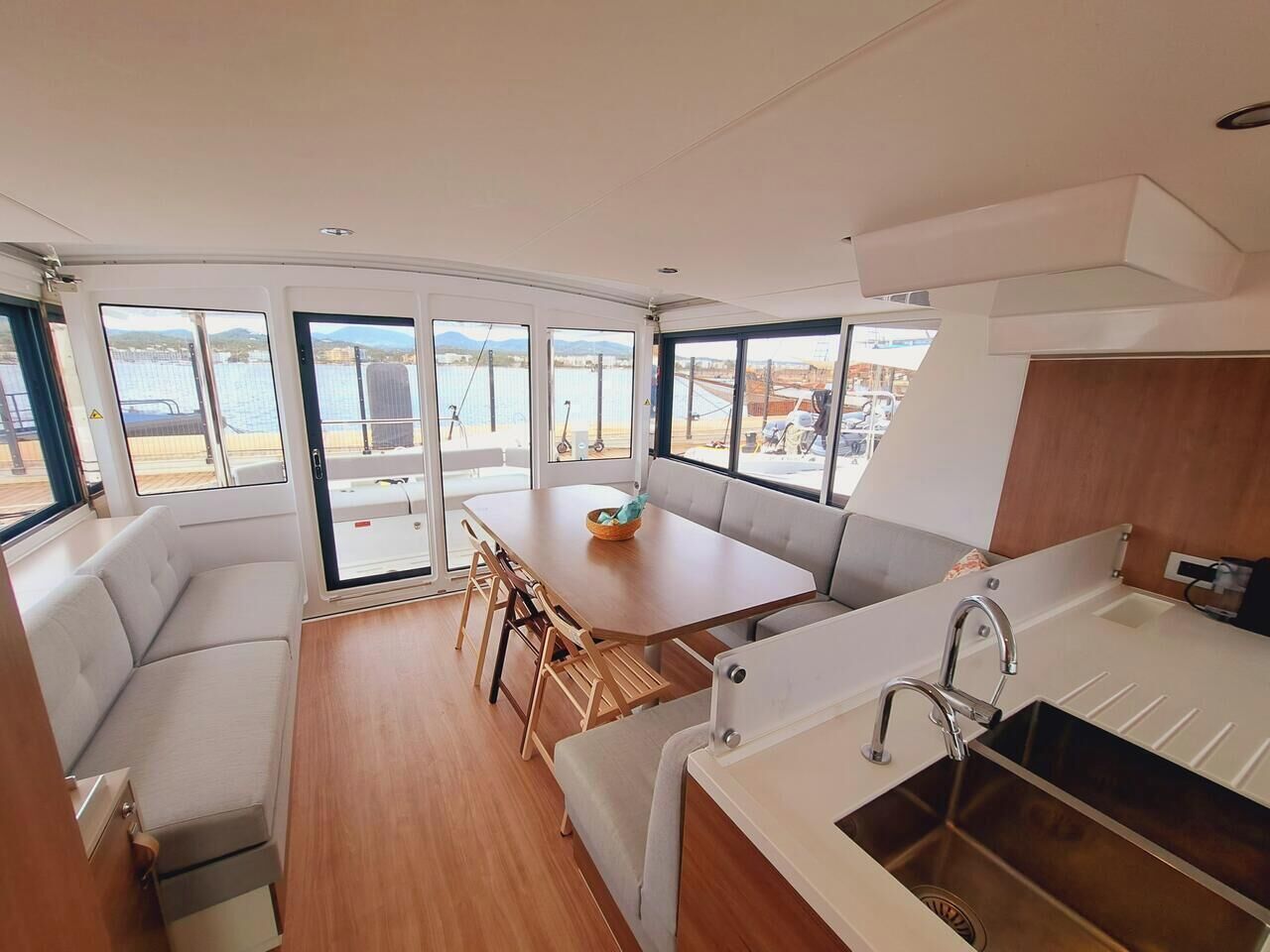 Un intérieur moderne comprenant un coin repas, une cuisine avec un évier et de grandes fenêtres offrant une vue sur l’eau.