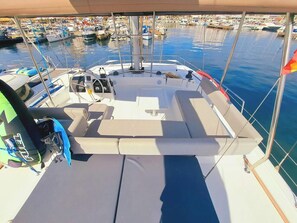 Ein Bootsdeck mit Sitzgelegenheiten, einem Steuerbord und Blick auf eine Marina mit weiteren Booten.