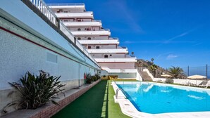 A swimming pool with a green artificial turf border, adjacent to a white building with multiple balconies. - GuestReady - Balcon de Amadores Sea View (Puerto Rico)