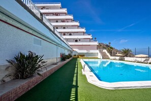 A swimming pool with a green artificial turf border, adjacent to a white building with multiple balconies. - GuestReady - Balcon de Amadores Sea View (Puerto Rico)