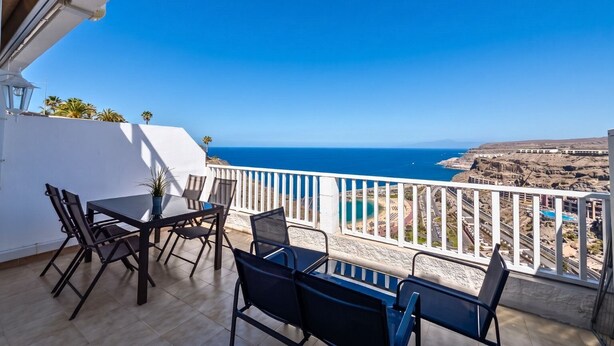 A balcony with a table and chairs, overlooking a coastal landscape with a clear sky. - GuestReady - Balcon de Amadores Sea View (Puerto Rico)