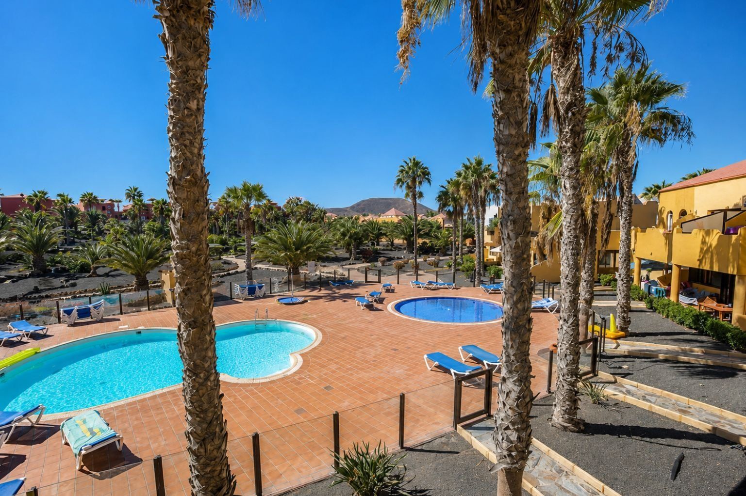 Un complexe hôtelier doté de plusieurs piscines, de palmiers et offrant une vue sur un paysage montagneux.
