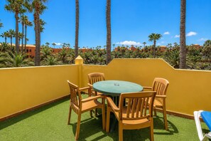 Eine Terrasse mit einem runden Tisch und vier Stühlen, umgeben von Palmen und Gebäuden im Hintergrund.