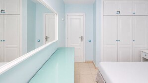Hotellihuone, jossa on lasipintainen työpöytä, raidallinen päiväpeite, valkoiset vaatekaapit ja suuri peili.