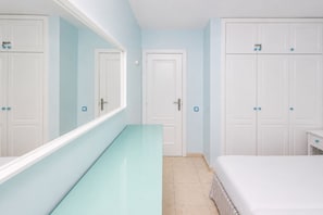 A hotel room with a glass-topped desk, a bed with a striped bedspread, white wardrobes, and a large mirror. - GuestReady - Modern Stay with Pool and Terrace (Corralejo)