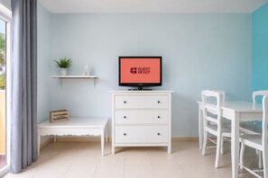 A modern room with a television displaying 'GUEST READY,' a white desk, a chair, a small shelf with a plant, and a bench. - GuestReady - Modern Stay with Pool and Terrace (Corralejo)